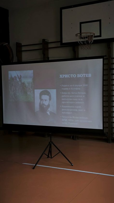 Ученици и възрастни наблюдават презентация в училищната зала.